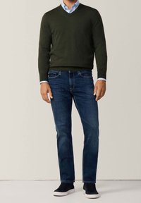 Pull à col en V vert foncé, chemise à col bleu clair, jean bleu et baskets montantes noires. Design simple, texture douce et coupe décontractée.
