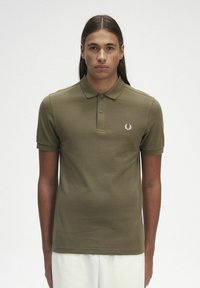 Polo shirt verde oliva con maniche corte e colletto classico. Presenta un piccolo logo bianco sul lato sinistro del petto. Tessuto in cotone liscio.
