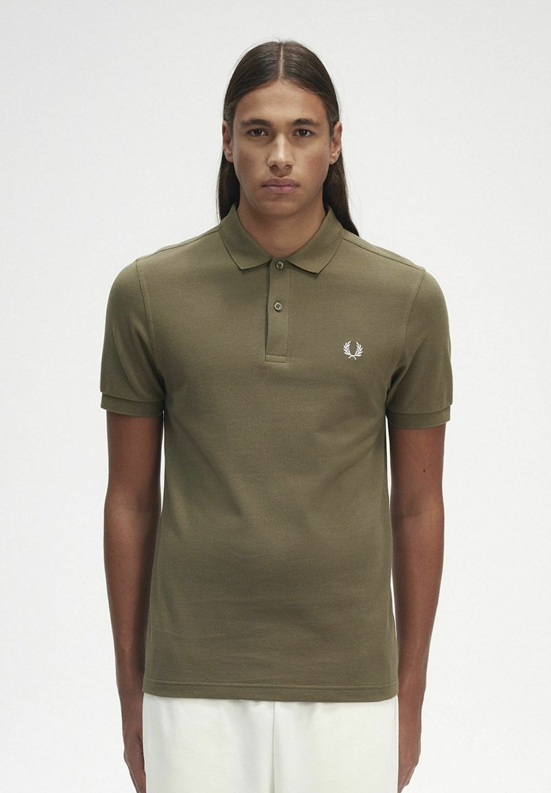 Polo shirt verde oliva con maniche corte e colletto classico. Presenta un piccolo logo bianco sul lato sinistro del petto. Tessuto in cotone liscio.