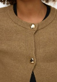 Rjav pleten pulover z rebrastim izrezom, z zlatimi gumbi v obliki srca in mehko teksturo. Vidna črna majica spodaj.