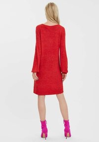 Robe rouge en tricot avec une coupe décontractée, manches longues évasées et un col en U, associée à des bottines rose vif à la cheville.