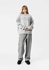 Sudadera oversized gris con el logo "MTV", combinada con pantalones gris holgados con cremallera lateral. Llevada con calzado negro texturizado.