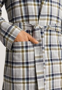 Kollad morgonrock i grått, vitt, marinblått och olivgrönt med knytning i midjan, långa ärmar och sidofickor. Tygets struktur ser lätt och linneaktig ut.