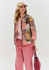 Pletená bunda s květinovými a kostkovanými vzory v růžových, zelených a žlutých odstínech. V kombinaci s růžovými manšestrovými kalhotami a béžovou kšiltovkou.