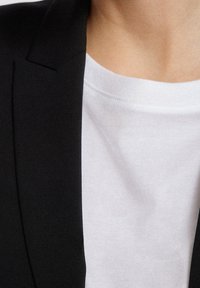 Svart kavaj med en strukturerad slag bredvid en enkel vit t-shirt. Kavajen har en slät yta, medan t-shirten har en mjuk bomullsliknande känsla.