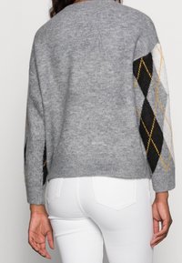 Grauer Strickpullover mit diamantähnlichen Mustern in Schwarz, Weiß und Gelb an den Ärmeln, rundem Halsausschnitt und geripptem Saum.