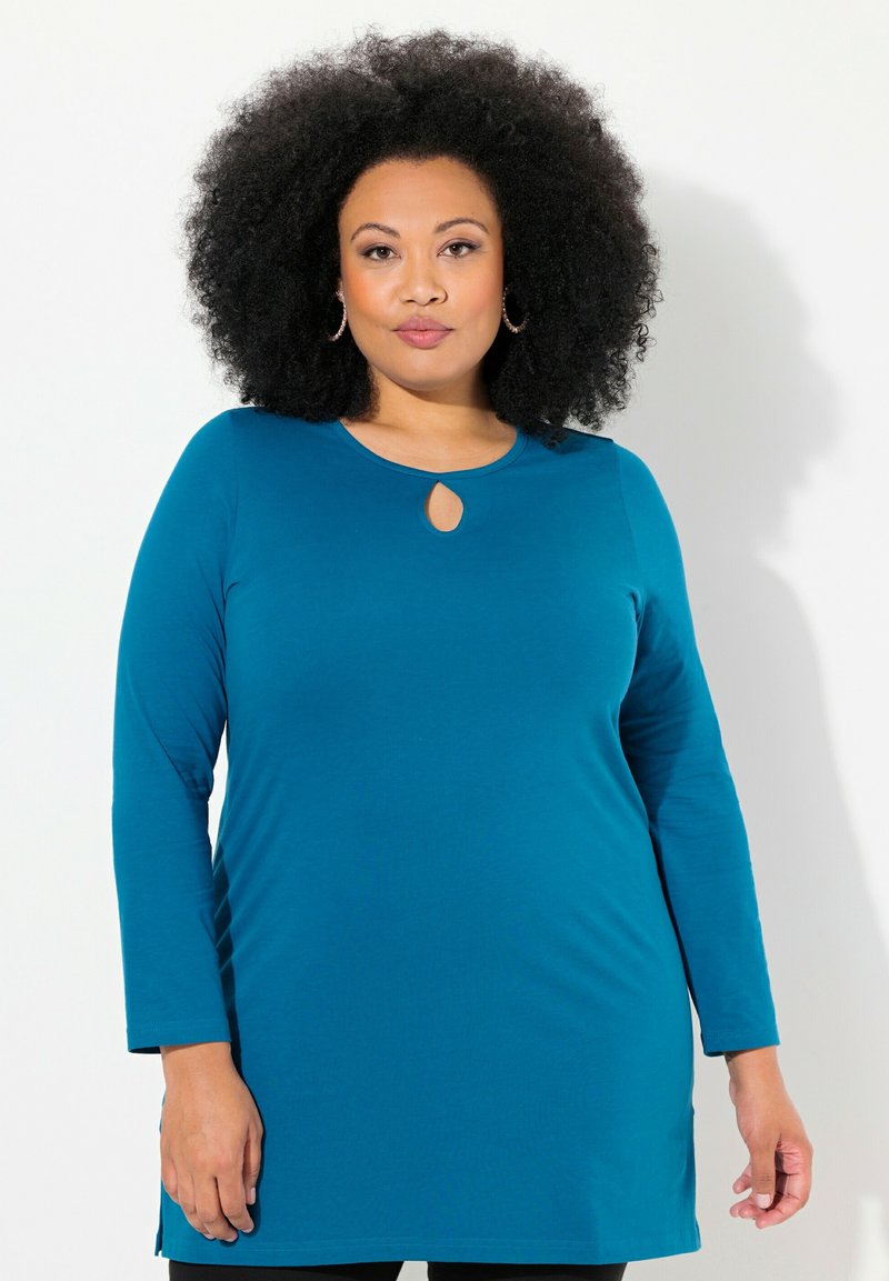 Tunique a maniche lunghe di color teal con dettaglio a chiave nel collo. Texture morbida, vestibilità comoda, spacchi laterali e orlo rotondo. Adatta per un abbigliamento casual.