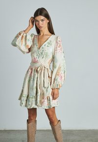 Wickelkleid aus hellbeigem Stoff, mit floralen Stickereien in Grün, Pink und Orange, puffärmel und einem gerafften Saum.