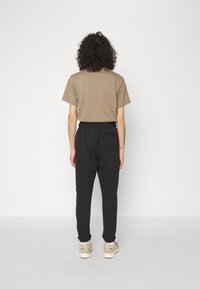 Brun bomullströja, kort ärm, avslappnad passform, matchad med svarta joggers med elastisk midja, som har en bakficka, bärs med ljusa sneakers.