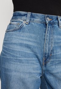 Jasnoniebieskie jeansy z denimu o prostym kroju, z wysokim stanem, pięcioma kieszeniami, kontrastowymi przeszyciami oraz zapięciem na metalowy guzik.