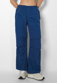 Blue lightweight pants with an elastic waistband, cargo pockets, and a loose fit. Made from smooth, breathable fabric. Textured surface.