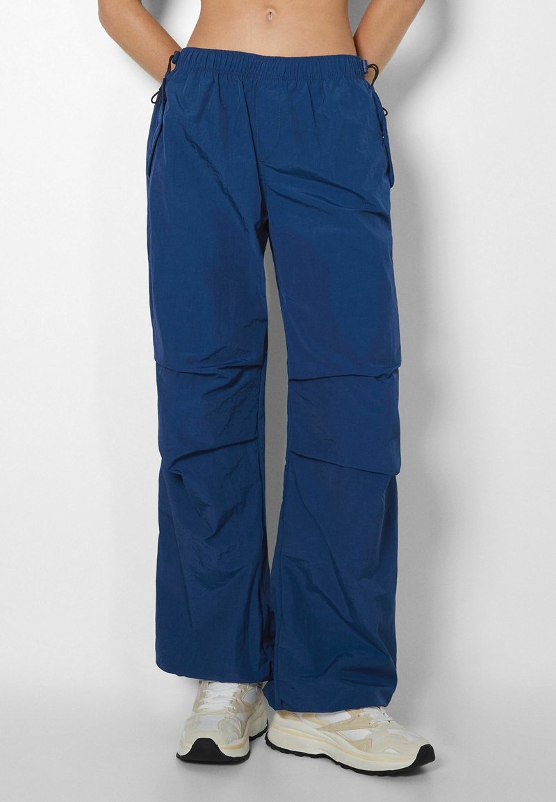 Blue lightweight pants with an elastic waistband, cargo pockets, and a loose fit. Made from smooth, breathable fabric. Textured surface.
