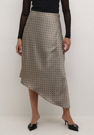 Asymetryczna satynowa spódnica w kolorze beżowym w czarne kropki. Gładka tekstura, długość do kolan z wysokim rozcięciem, w zestawieniu z czarnymi butami w szpic.