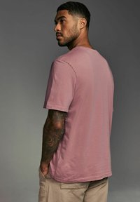 Tricou cu mânecă scurtă, guler rotund, din bumbac roz pal, cu o croială lejeră și o textură ușoară, asociat cu pantaloni scurți bej.