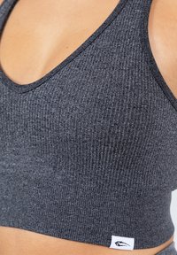 Top corto de canalé gris con escote en V y etiqueta de logo cosida. Textura de tela suave, diseño ajustado y sin cierres visibles.