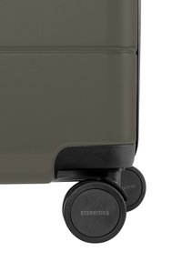Valise rigide de couleur vert olive atténué avec surface texturée, équipée de roues noires et de marquages sur les roulettes, au design compact.