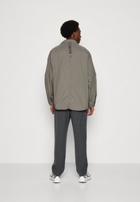 Light gray oversized jacket with textured fabric, long sleeves, and a back strap detail. Paired with dark gray trousers and white sneakers.