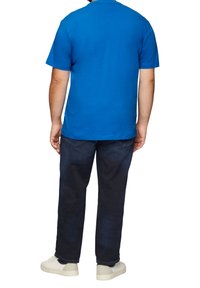 Blue short-sleeve T-shirt, cotton material, round neck, worn with dark denim jeans and white sneakers, viewed from the back.