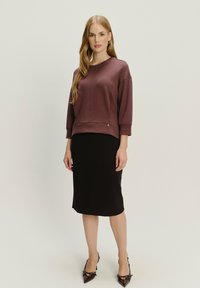 Sudadera morada oscura con un corte relajado y hombros caídos, combinada con una falda lápiz negra. El conjunto se completa con unos tacones negros puntiagudos.
