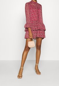 Floral-patterned, pink dress with long sleeves and tiered ruffle detail. Paired with a small light pink handbag and strappy sandals.