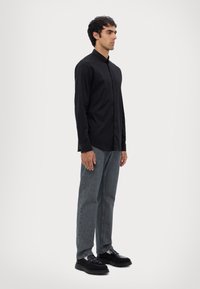 Zwarte lange mouw button-up shirt met een relaxte fit, gecombineerd met grijze rechte jeans en zwarte schoenen met een chunky zool.