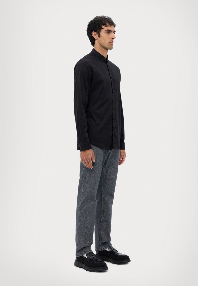 Zwarte lange mouw button-up shirt met een relaxte fit, gecombineerd met grijze rechte jeans en zwarte schoenen met een chunky zool.