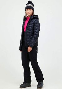 Mustat untuvatakki, jossa on huppu, tikattu design ja vetoketjukiinnitys, käytetty vaaleanpunaisen topin ja mustien housujen päällä, yhdistettynä mustiin saappaisiin ja pipoon.