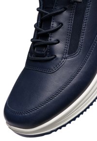 Nahaufnahme eines marineblauen Leder-Sneakers mit schwarzen Schnürsenkeln, detaillierter Naht, elastischem Seitenpanel und weißer, strukturierter Sohle.