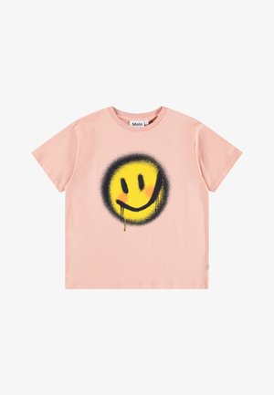 Roza bombažna majica s kratkimi rokavi, ki ima velik črno-rumeni nasmejan obraz, narejen s sprejem, z kapljicami barve in okroglo ovratnikom.