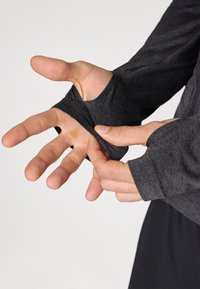 Long-sleeve, dark gray athletic shirt with thumbhole cuffs, featuring a smooth texture and fitted design, emphasizing hand movement.