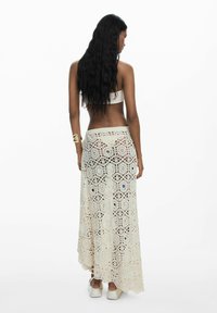 Háčkovaná sukňa v odtieňoch ecru, s kvetinovými vzormi a mierne rozšíreným strihom. Voľný strih s vysokým pásom a asymetrickým lemom.