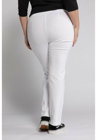 Witte fitted broek met een gladde textuur, ontworpen met twee achterzakken en gecombineerd met zwarte sneakers met een witte zool.