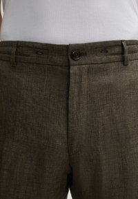 Pantalons marron foncé en tissu texturé, avec fermeture à bouton, passants de ceinture et un motif à carreaux discret.