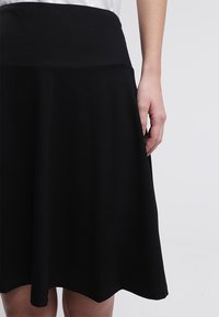 Schwarzer Rock mit einem taillierten Bund, ausgestellter Silhouette und glatter Textur, der knielang ist und ein einfaches und sauberes Design präsentiert.