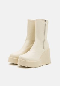 Botine albe din piele cu o talpă platformă masivă, având un fermoar pe lateral și o textură netedă. Design simplu cu detalii cusute.