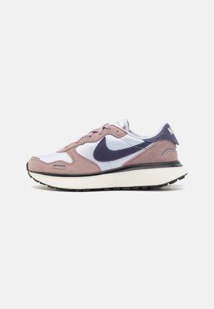 Niski profil butów sportowych z białymi i liliowymi nakładkami z zamszu, ciemnoniebieskim logo Nike i grubą białą podeszwą z czarnym bieżnikiem na jednolitym tle.