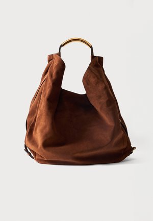 Sac à main souple en daim marron avec une poignée supérieure dorée structurée et une bandoulière réglable sur un fond clair uni.