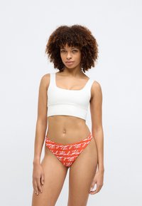 Dvoudílné plavky s bílým crop topem se čtvercovým výstřihem a oranžovými bikinami se spodními kalhotkami s bílým ručně psaným vzorem. Hladká textura.