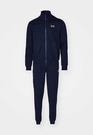Completo sportivo blu navy realizzato in morbido tessuto, con giacca con zip e colletto alto e pantaloni affusolati abbinati. Logo su entrambi i pezzi.