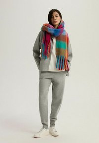 Szary zestaw bluzy i spodni dresowych, miękka tekstura. Kolorowy szalik w paski w odcieniach różowym, pomarańczowym, niebieskim i zielonym. Białe, niskie trampki.
