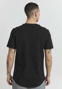 Camiseta de algodón negra con mangas cortas, escote redondo y corte recto. La tela parece suave, con un diseño liso.