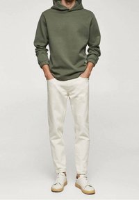 Sweat à capuche vert olive avec poignets élastiques, associé à un pantalon crème fuselé et des baskets blanches avec semelles beige.