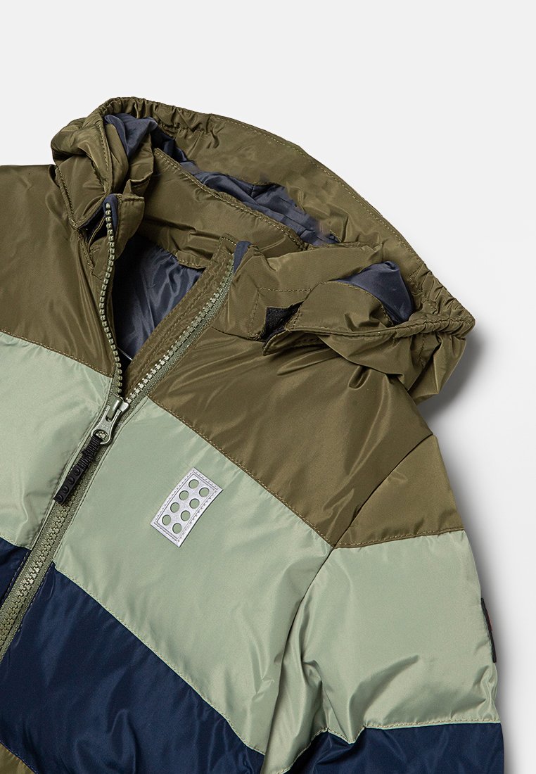 Veste matelassée avec un design en blocs de couleurs olive, vert clair et bleu marine. Comprend une capuche et une fermeture éclair sur le devant avec un logo.