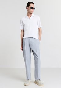 Polo shirt bianco a maniche corte con righe abbinate a pantaloni grigi chiari con pieghe e scarpe grigie; occhiali da sole completano il look.