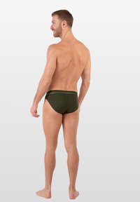 Groene heren zwemboxers met een gladde textuur en een elastische tailleband, die een strakke pasvorm tonen vanuit een zijkant.