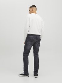 Jeans de mezclilla oscura con corte slim, con bolsillos traseros y un lavado sutil. Combinados con una camisa blanca de manga larga y zapatos deportivos negros.
