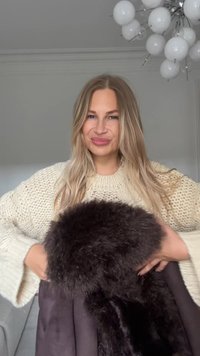 Black fur coat with a plush collar, paired with a chunky knit cream sweater. The coat has a sleek design and smooth texture.