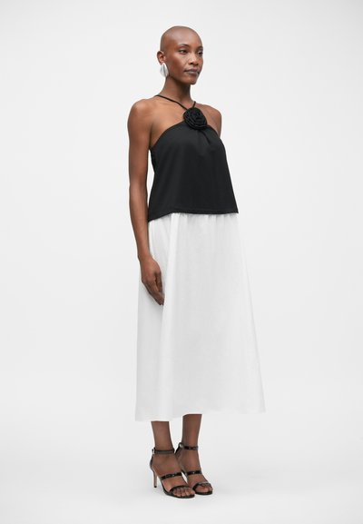 Top noir à encolure halter avec détail en rose, jupe blanche fluide et sandales noires à lanières. Tissu lisse avec des couleurs contrastantes et un design simple.