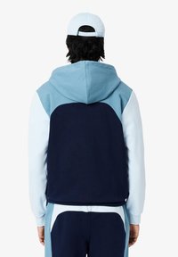 Sweat à capuche bleu et marine avec un design en blocs de couleur. Caractérisé par une texture douce et une coupe décontractée, avec une poche kangourou.