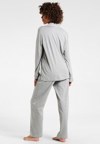 Camisola de pijama cinza de mangas longas com colarinho, combinada com calças largas cinzas. Tecido macio e leve com um corte relaxado. Sem padrões ou detalhes.